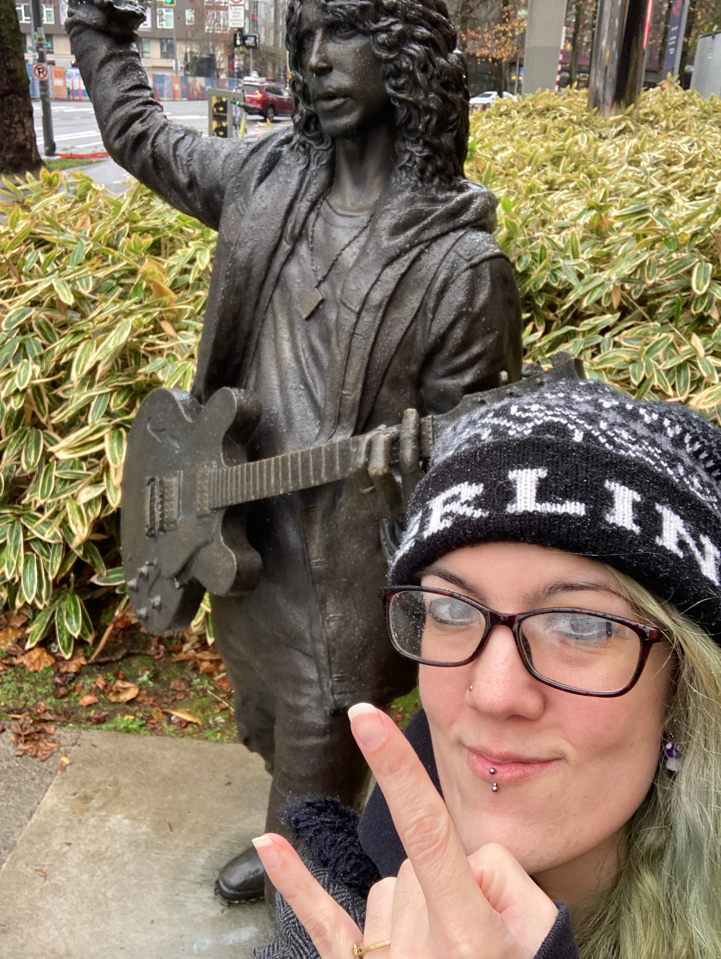 Image of Jen wearing a Berlin beanie and standing next to a statue of Chris Cornell.