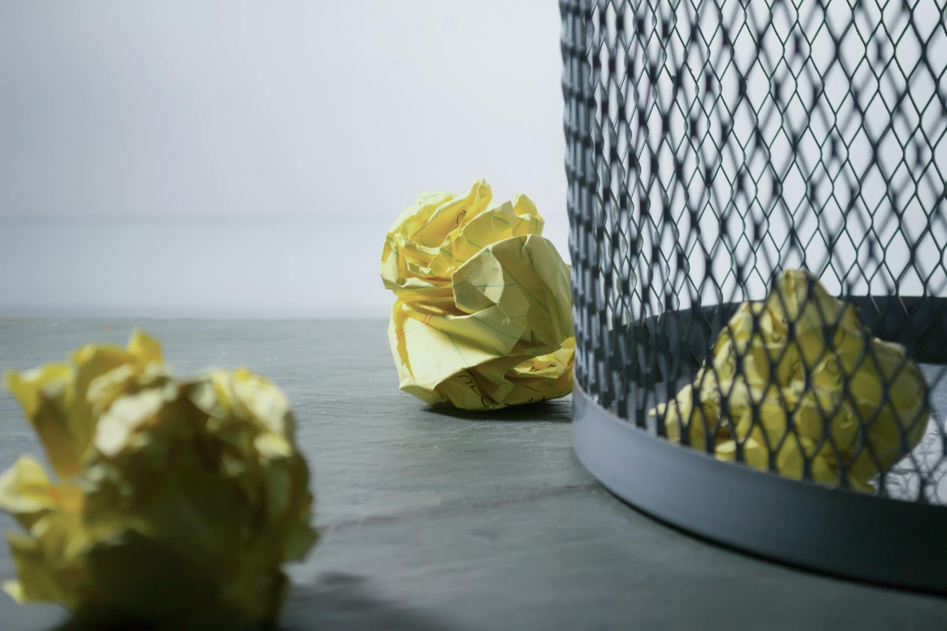 Image of crumpled piece of paper next to a garbage can.